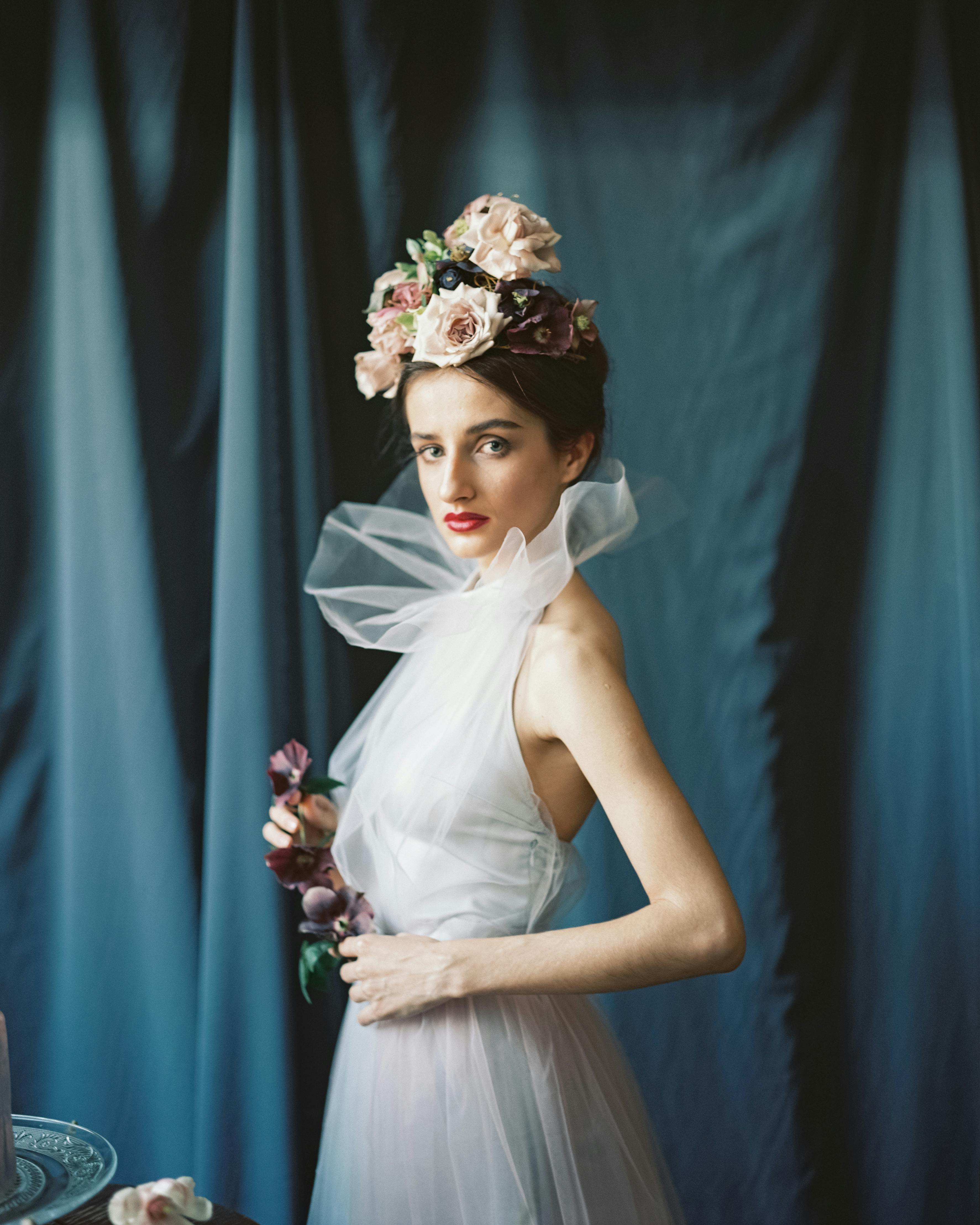 Portrait of a woman in sheer fabric and floral headpiece, embodying high fashion elegance.