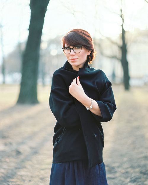 Free Portrait of a young woman smiling in a park during fall, wearing a black coat and glasses. Stock Photo