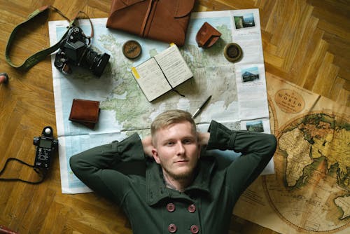 Free A Man Lying on the Floor Over World Maps and Other Travel Tools Stock Photo