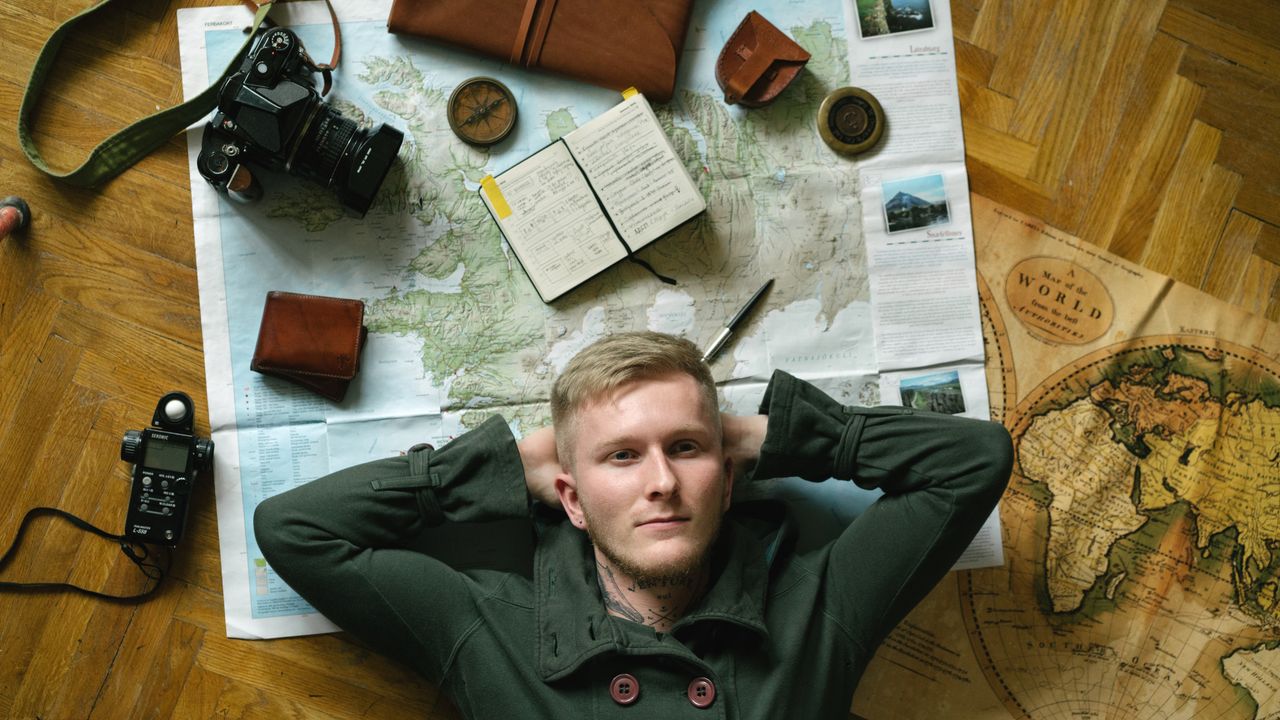 Young traveller planning a trip, surrounded by maps, camera, and notebook.