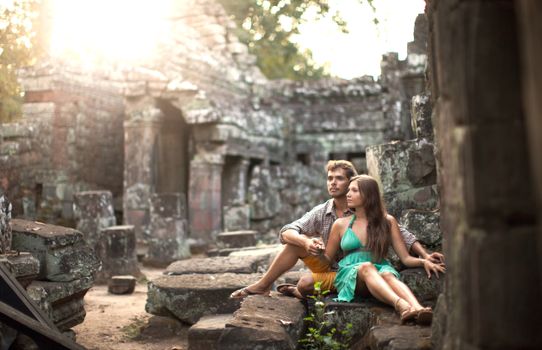 A couple sits together at ancient stone ruins, embracing affection and history.