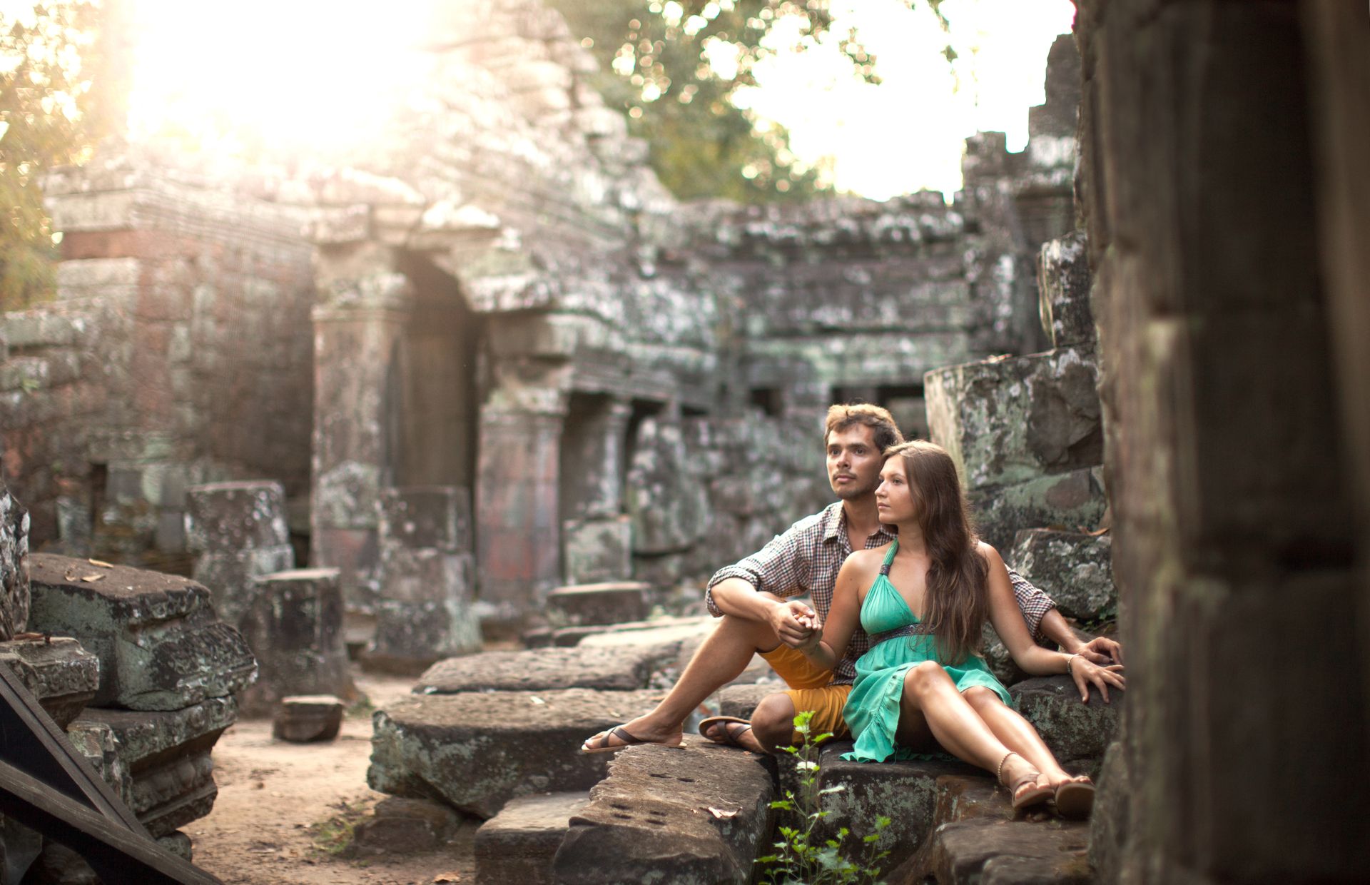 A couple sits together at ancient stone ruins, embracing affection and history.
