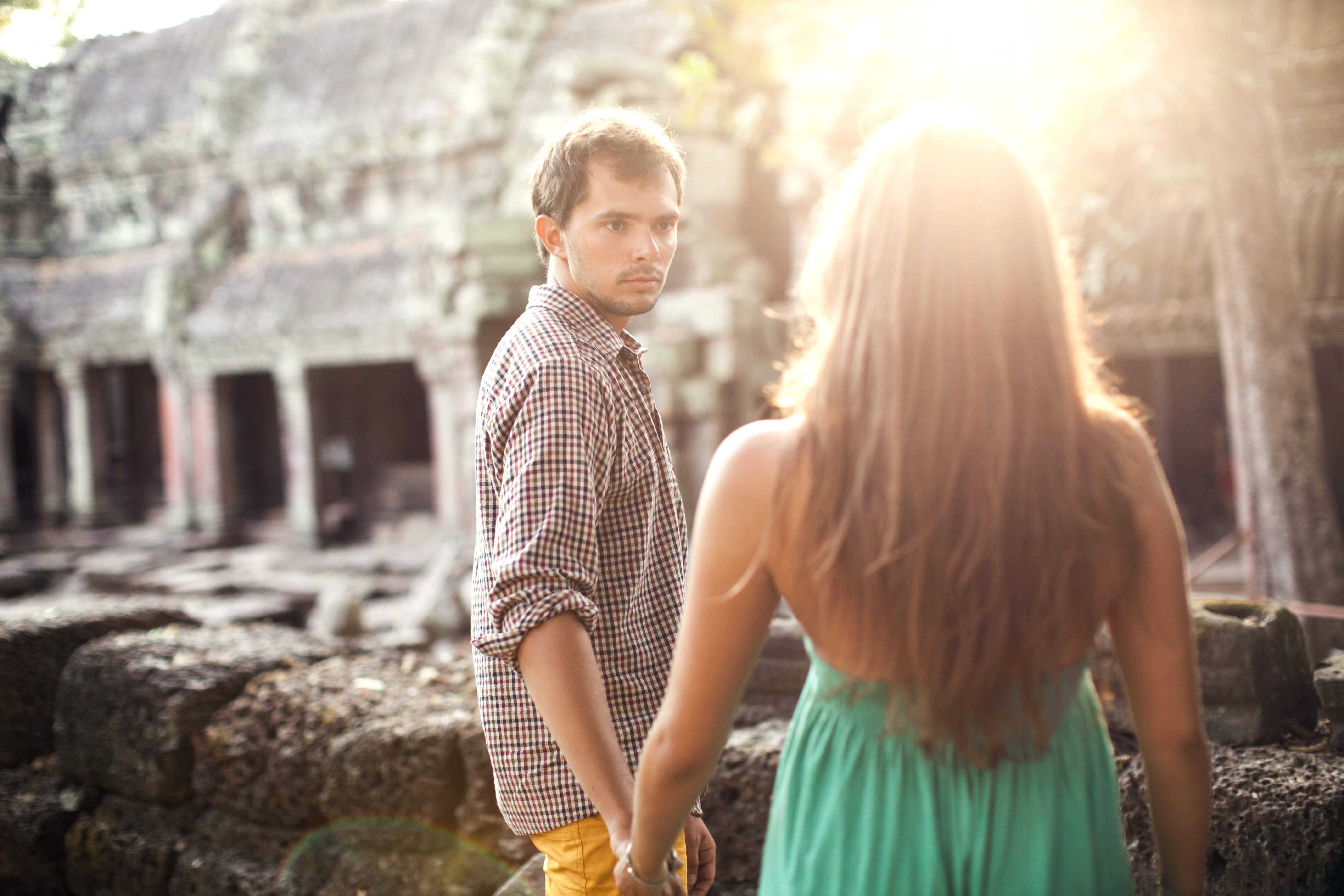 A young couple holding hands explores ancient temple ruins in sunlight, depicting romance and adventure.