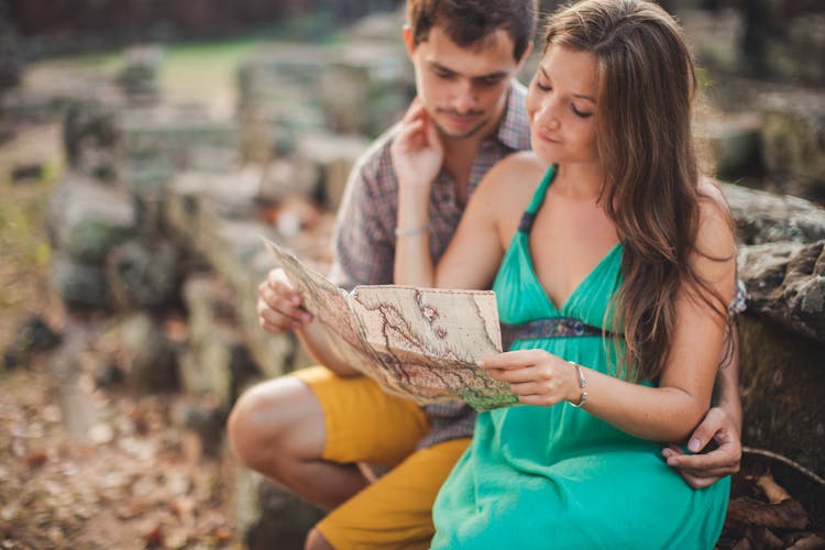 A Couple Sitting Close Together Looking At A Map