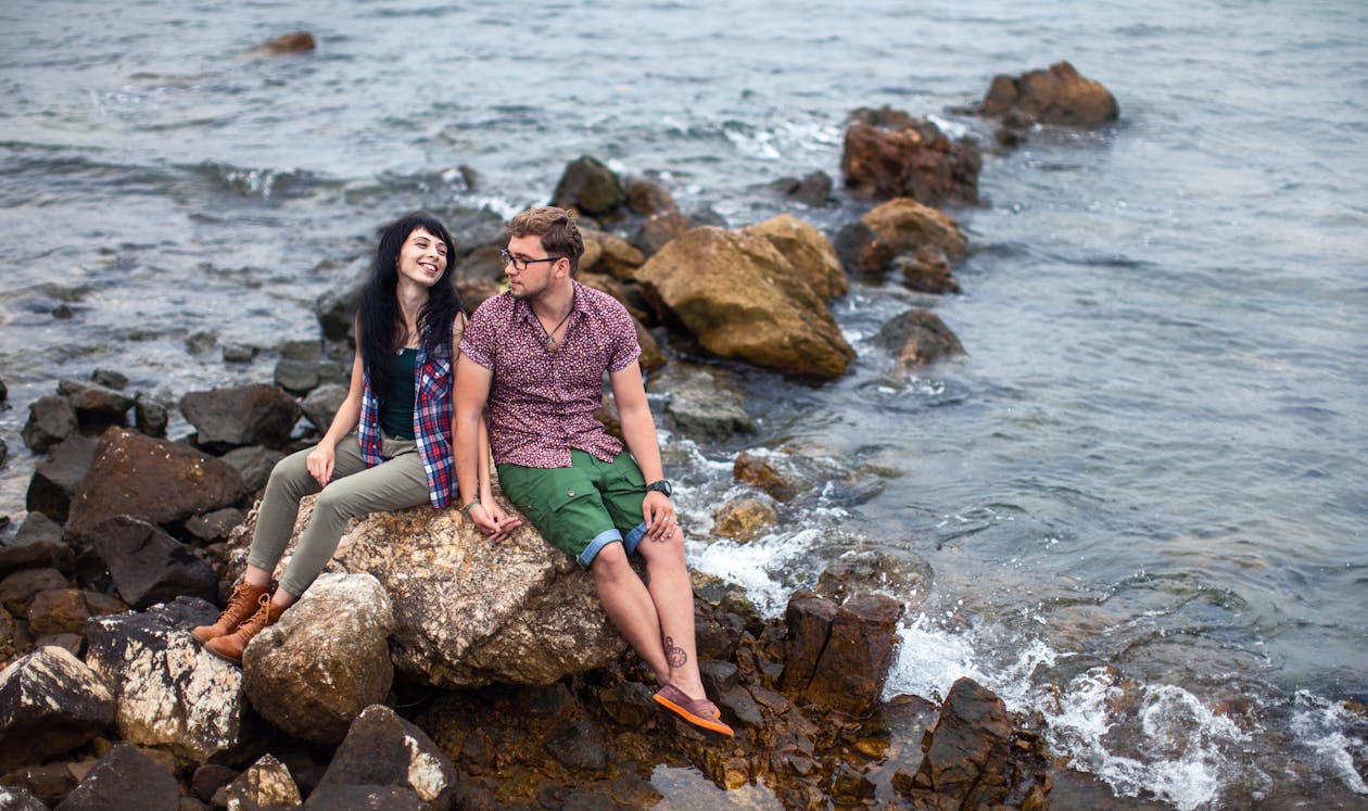 Free A Couple Sitting on a Rock Near Body of Water Stock Photo