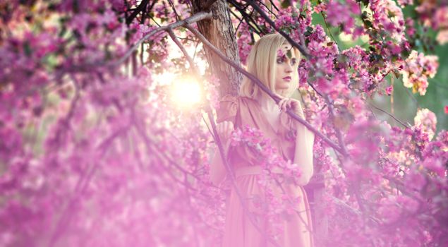 A woman surrounded by pink blossoms in springtime, capturing serene beauty.