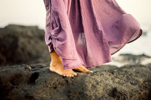 一位赤脚的人穿着飘逸的紫色裙子，站在多岩石的海滩上，散发着自然的优雅