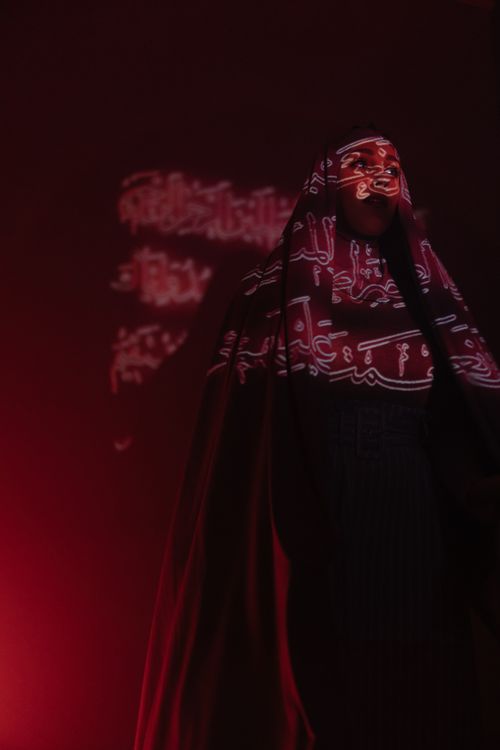 Free A woman in traditional clothes with Arabic calligraphy projections in a dimly lit room, creating a mysterious ambience. Stock Photo