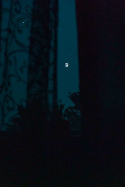 A dramatic view of a full moon and stars through a silhouetted window at night.