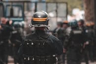 Back view of anonymous policeman in helmet and bulletproof vest maintaining law and order while standing on city street