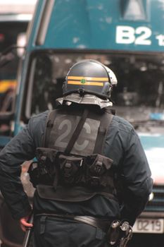 Back view of faceless police officer wearing helmet and protective vest with gun and baton standing in front of police van