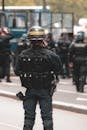 Back view of armed police officer wearing uniform with helmet and body armor performing duties while standing on road