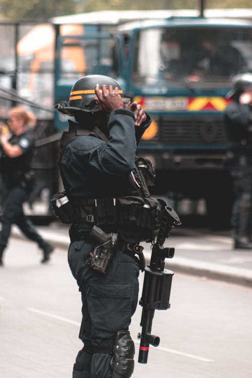 Free Side view of armed African American policeman with guns wearing protective helmet and vest controlling street Stock Photo