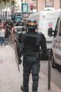 Back view of faceless police officer wearing protective uniform with helmet and shield walking towards crowd on sidewalk