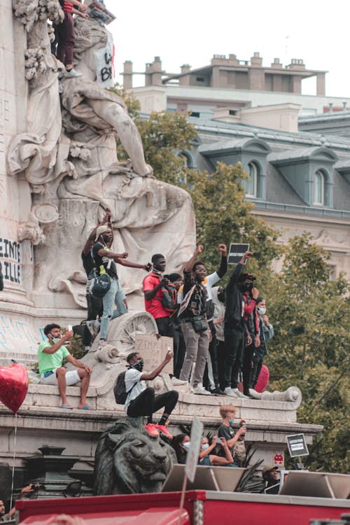 Free Group of diverse protesters with hands up and sign standing on monument and making demands Stock Photo