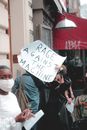 Anonymous female in protective mask participating in demonstration and holding placard saying Rage against the machine