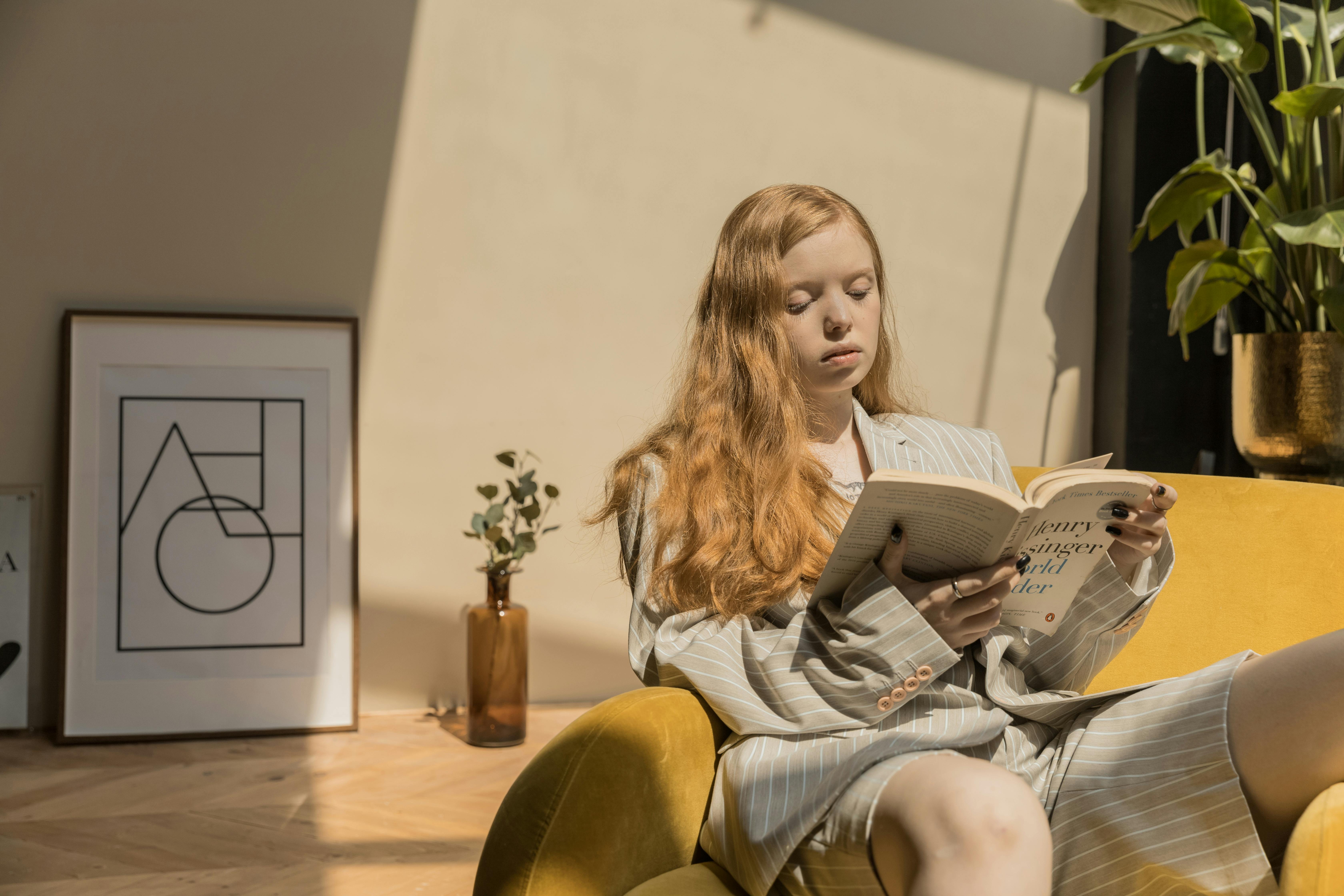 a young woman sitting on a yellow chair reading a book