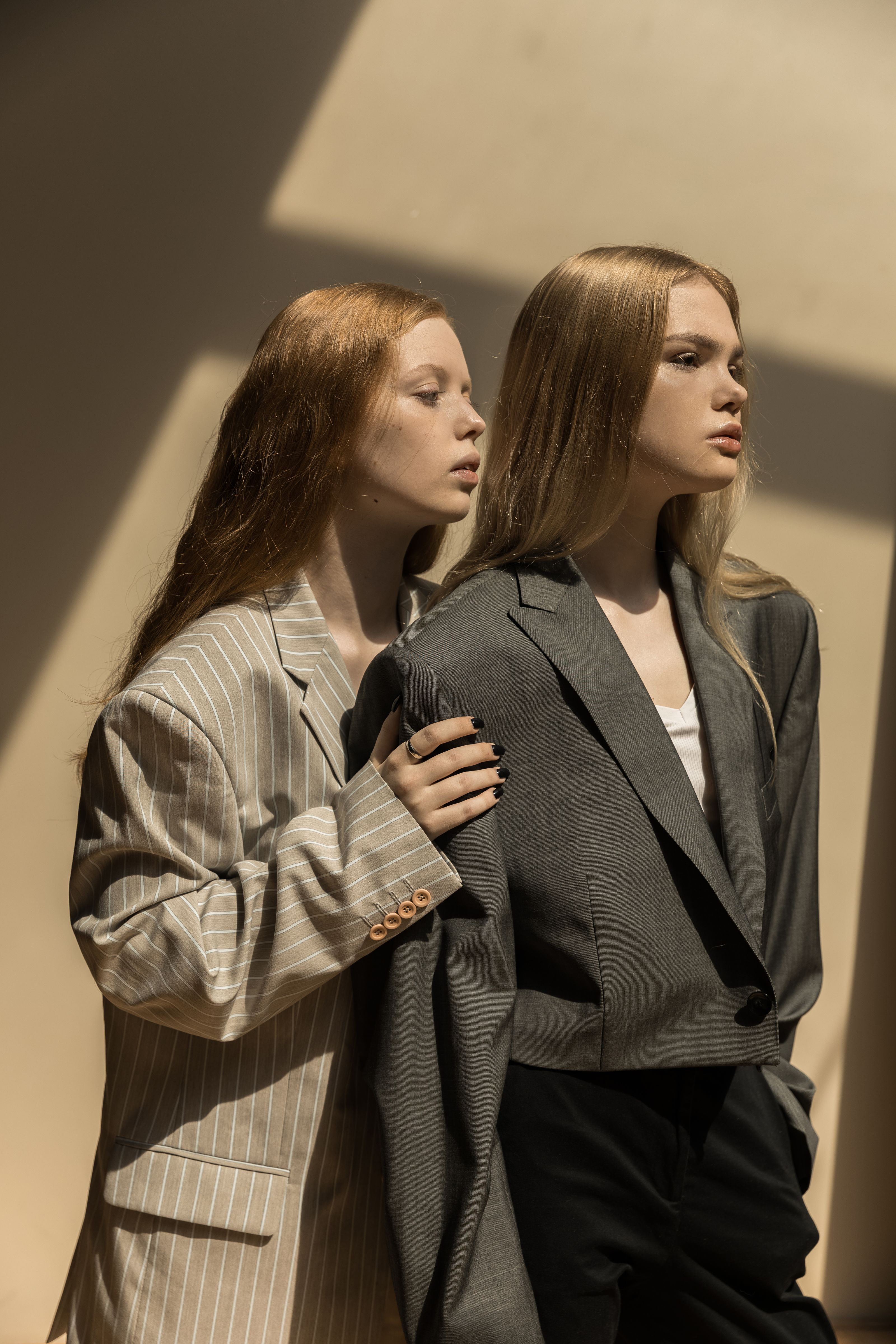 Duas jovens em trajes estilosos posando elegantemente com iluminação dramática em ambientes internos.