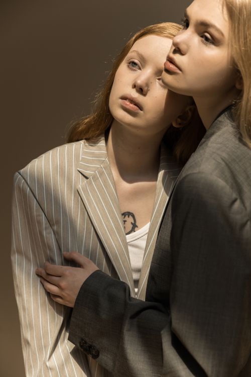 Free A graceful portrait of two women in fashionable suits, embracing gently in soft sunlight. Stock Photo