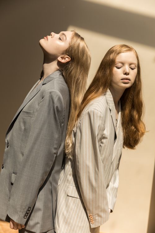 Free Artistic portrait of two women in stylish suits posing back to back under sunlight indoors. Stock Photo