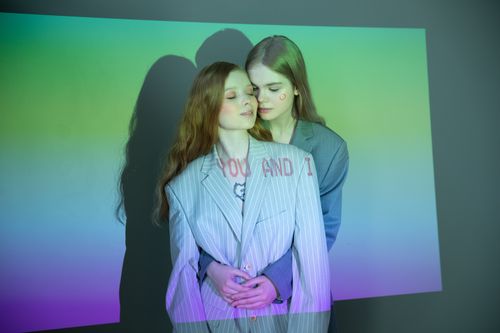 Free Two women embracing in a studio with colorful light projections and text. Stock Photo