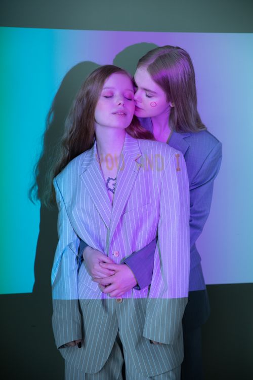 Free Two women embrace in stylish suits with colorful light projections, symbolizing love Stock Photo