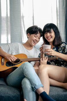 两个女人在室内喝着咖啡，弹着吉他，在沙发上享受快乐的时光