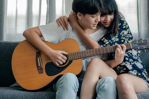 Free Woman Playing Guitar While Being Hugged by a Person Stock Photo