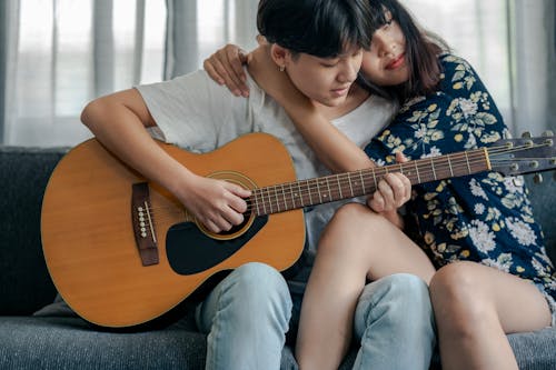 Free Woman Sitting on Sofa Playing Guitar Beside a Person Stock Photo