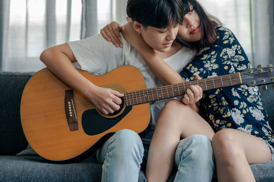 Lesbian couple shares a tender moment while playing guitar together at home.