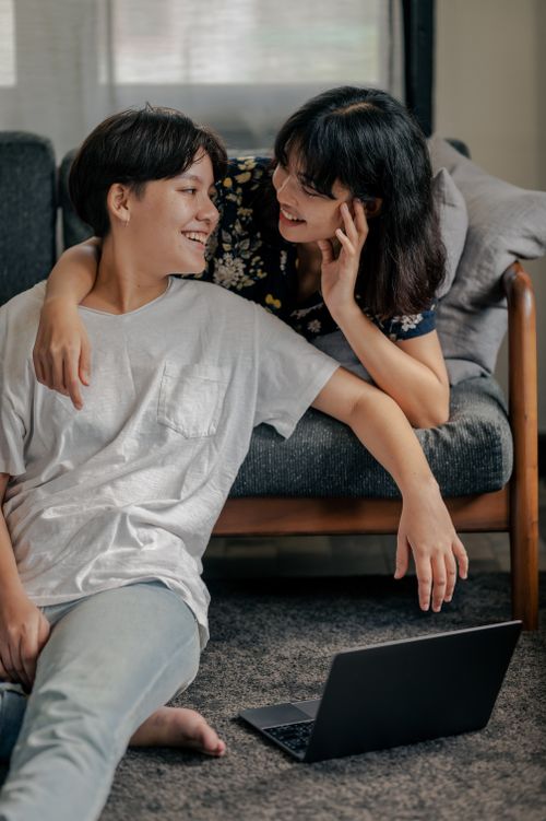 Free A joyful couple sitting together, sharing a moment on the floor with a laptop. Stock Photo