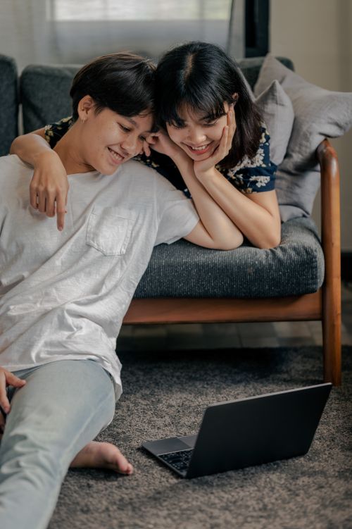 Free Smiling couple relaxing indoors, watching something on a laptop, showcasing affection and togetherness. Stock Photo