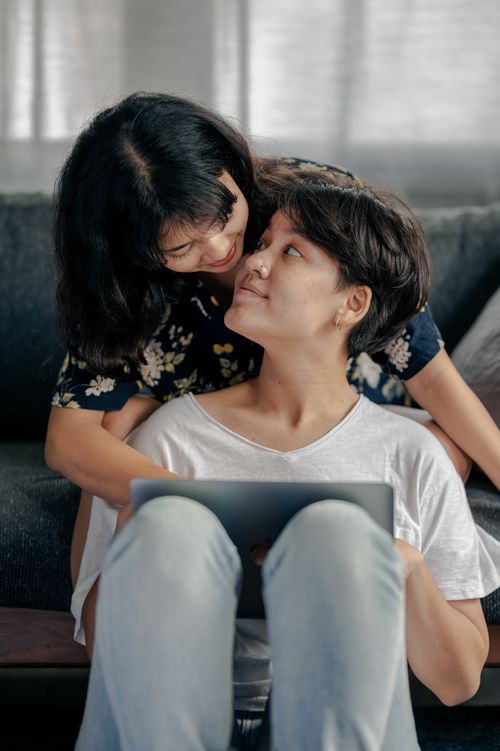 Free Two women sharing an affectionate moment while using a tablet at home. Stock Photo