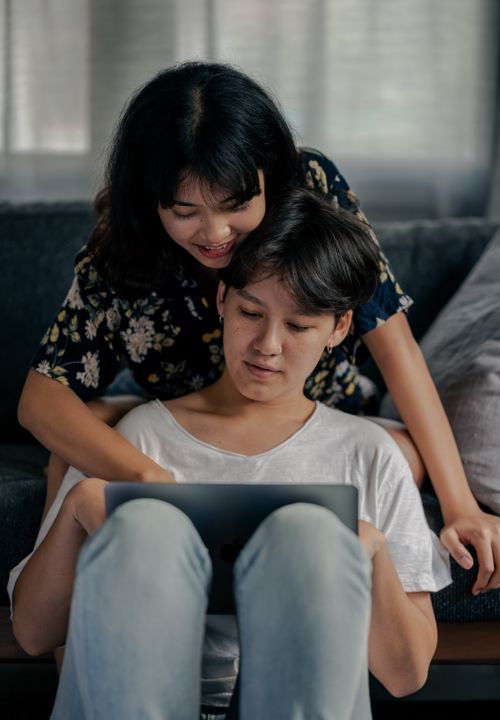 Free A happy couple sitting on the couch, smiling and using a laptop indoors. Stock Photo