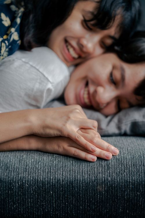 Free A joyful couple lying close together on a couch, smiling and holding hands, capturing a moment of affection and love. Stock Photo