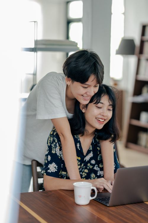 Free A joyful couple embraces while using a laptop indoors, capturing a warm and intimate moment together. Stock Photo