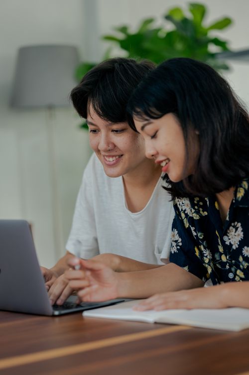 Free Two women smiling and collaborating on a laptop at home office desk. Stock Photo