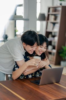 一对情侣微笑着拥抱，在室内的桌边一起享用咖啡，桌上放着一台笔记本电脑
