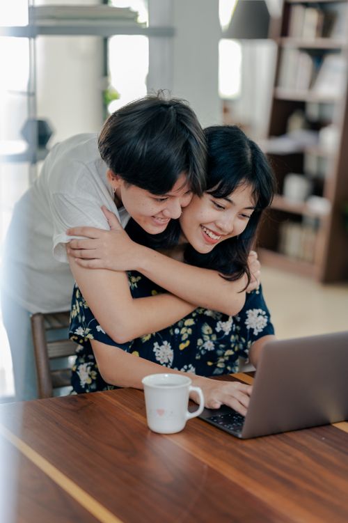 Free Couple embraces while working on laptop, enjoying remote work together. Stock Photo