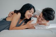 一对年轻夫妇在卧室里用智能手机快乐地分享了一个瞬间