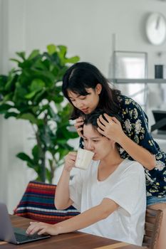 两个女人在室内喝着咖啡，其中一人使用着笔记本电脑，她们温暖地拥抱在一起