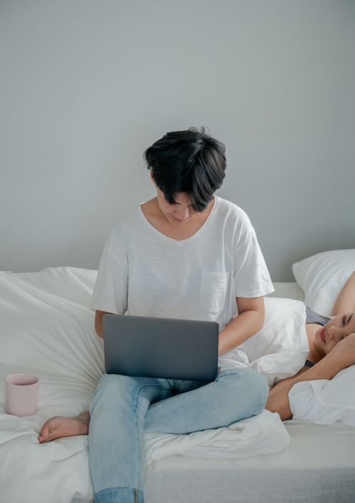 Free A couple relaxing on a bed, one using a laptop. Calm and cozy atmosphere. Stock Photo