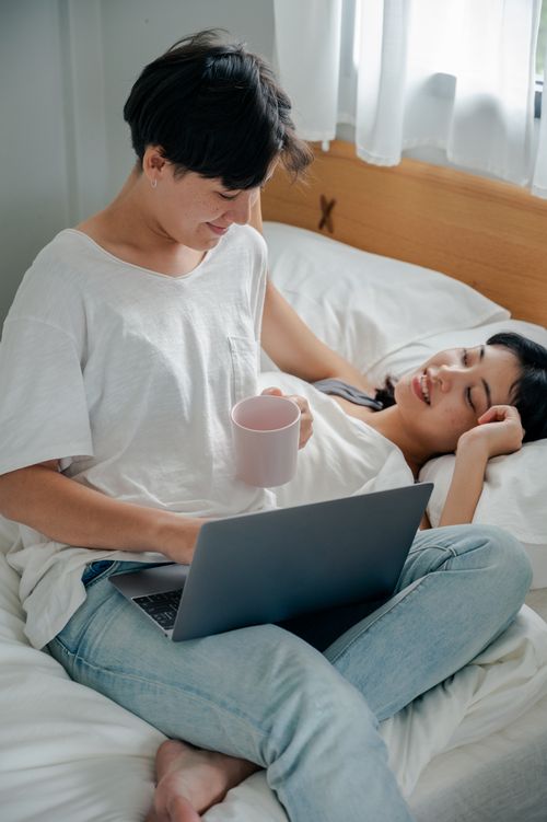 Free A loving couple enjoying a peaceful morning in bed with coffee and a laptop. Stock Photo