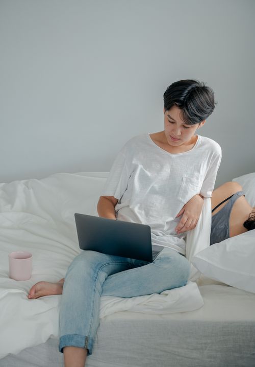 Free Young woman on bed working on laptop. Cozy and calm indoor setting. Stock Photo