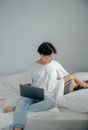 在一个舒适的卧室里，一个女人正用笔记本电脑工作，她的伴侣睡在一旁