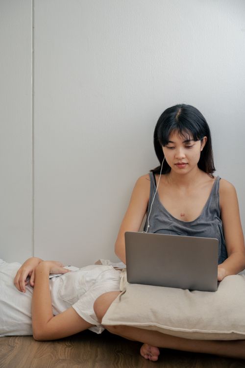 Free Two women relaxing indoors, one lying down while the other uses a laptop, listening to music. Stock Photo