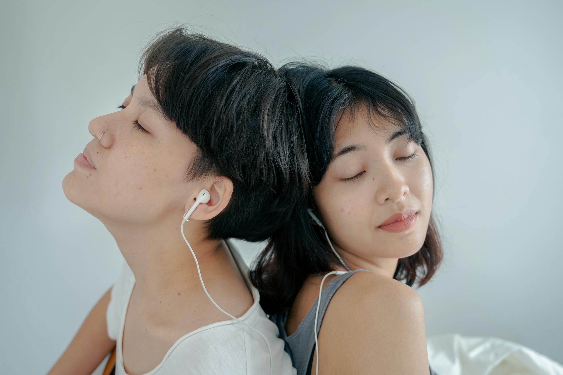 Two women with earphones share a peaceful moment, eyes closed, lost in music.