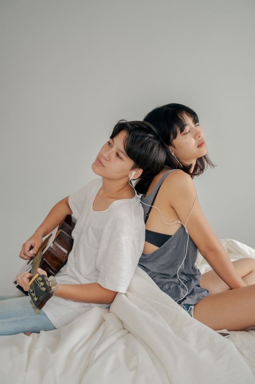 Free A couple sitting together on a bed, sharing music and playing guitar, evoking a sense of love. Stock Photo
