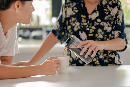 Two people sharing a morning coffee, one pouring into a mug, indoors.