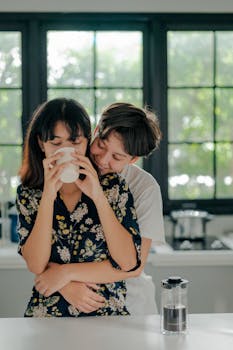 Two women embracing in a kitchen, sharing a tender moment while sipping coffee.